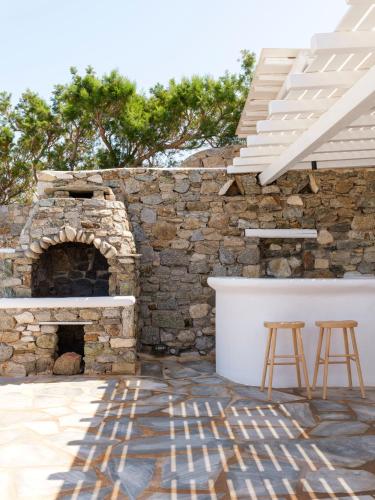 a patio with a stone fireplace and two stools at Aqua Lumen Private Pool Villa, Mykonos in Agios Ioannis Mykonos
