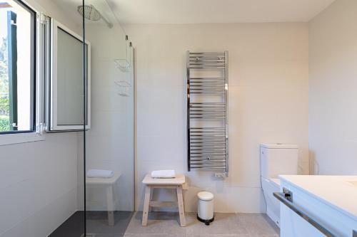a white bathroom with a glass shower and a stool at Finca Es Coste by Rentallorca in Pollença