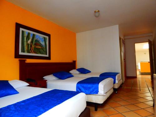 two beds in a hotel room with orange walls at Hotel Castillo Real in Armenia
