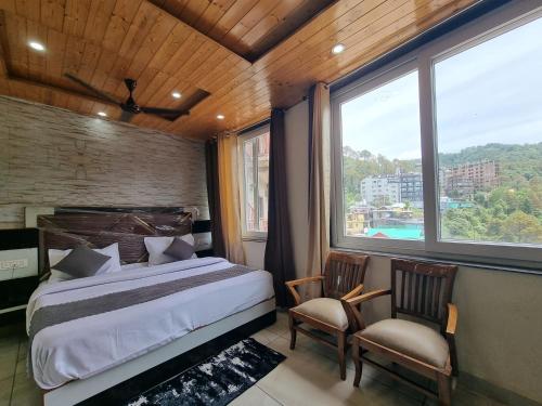 a bedroom with a bed and two chairs and a large window at Hotel Rajinder Prasth in Dalhousie