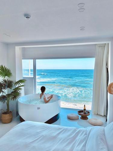 a woman sitting in a bath tub in a bedroom with the ocean at Gangneung The View Pension in Gangneung