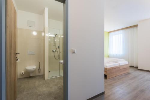 a bathroom with a shower and a toilet and a bed at Sleepin Premium Motel Loosdorf in Loosdorf