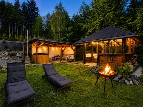 a cabin with two chairs and a fire in the yard at Biały Domek Świerczek - Jacuzzi, Balia Ruska SPA, Rowery, Altana i Grill w Słopnice in Słopnice