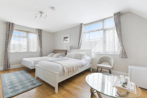 a white bedroom with two beds and a glass table at Katolondonhaus in Mitcham