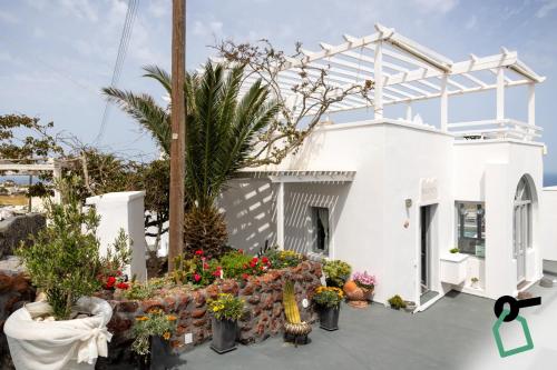a white house with flowers and plants in front of it at Hotiday Santorini Seafront in Santorini