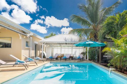 a swimming pool with chairs and an umbrella next to a house at Villa Ti'Palm in Saint-François