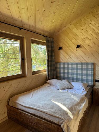 a bed in a wooden room with two windows at Apartament pod Świerkami in Witów