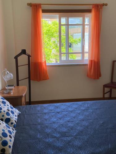 a bedroom with a bed and a window with orange curtains at Caparica Sol&Mar Apartment in Costa da Caparica