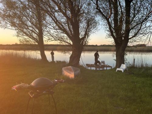 a couple of people standing around a picnic table next to a lake at Reetdachhaus direkt am Wasser in Breiholz