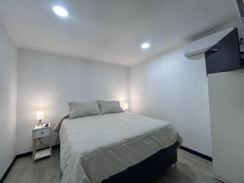 a white bedroom with a bed and a night stand at Cabañas Vista Mar in Los Vilos