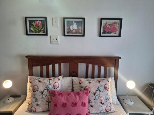 a bed with pink pillows and three pictures on the wall at Protea in Britannia Bay