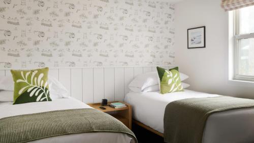 two beds in a room with white walls and green pillows at The Penny Lane in Hampton Bays