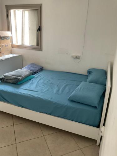 a bed with blue sheets in a room with a window at באר מרים in Ashkelon