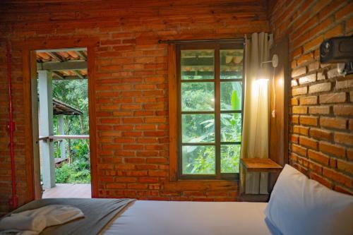 a bedroom with a brick wall with a bed and a window at Pousada Alto Pirapitinga in Resende