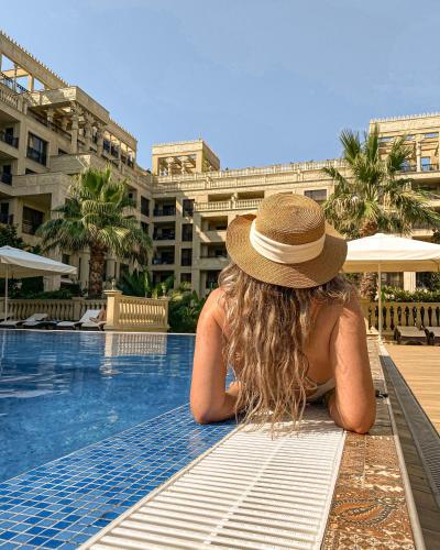 a woman in a hat sitting on a bench next to a swimming pool at Argisht Partez Hotel ALL INCLUSIVE & BEACH BAR REBLS in Golden Sands