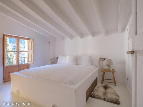 a white bedroom with a white bed and a window at C'an Llum in Deia