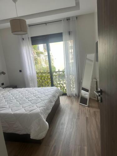 a bedroom with a bed and a large window at Joli appartement à Tamaris in Dar Bouazza