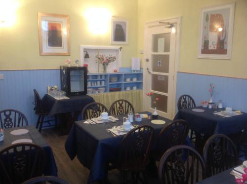 a dining room with blue tables and chairs and a tv at Cleasewood Guest House in Great Yarmouth