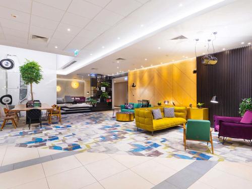 a lobby with a yellow couch and tables and chairs at Mercure Warszawa Grand in Warsaw