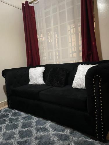 a black couch with pillows in front of a window at Nadine's Enclave in Kisii