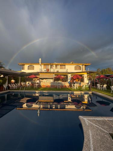a rainbow in the sky over a house with a pool at Hosteria Casa Silva in Checa