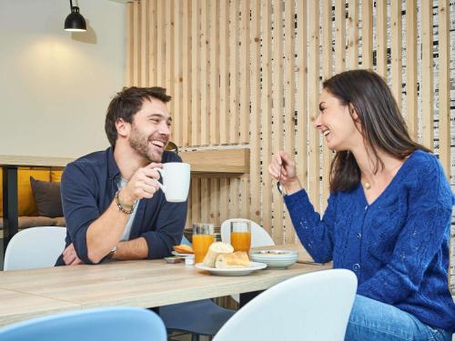 a man and woman sitting at a table drinking coffee at Aparthotel Adagio Access Paris Saint-Denis Pleyel in Saint-Denis