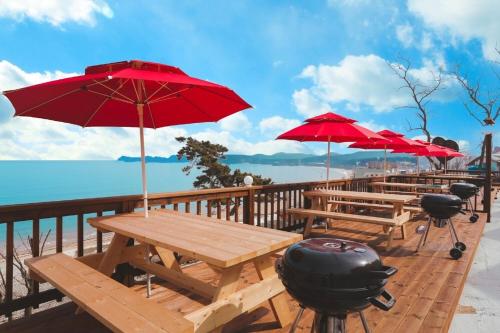 a picnic table with red umbrellas and a grill at Nuhrang Nahrang in Taean