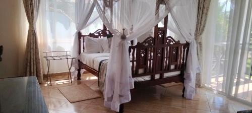 a bedroom with a canopy bed with white curtains at Blue Water Resort in Diani Beach