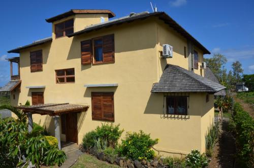 a yellow house with wooden windows and a roof at La Maison Soleil in Trou dʼ Eau Douce