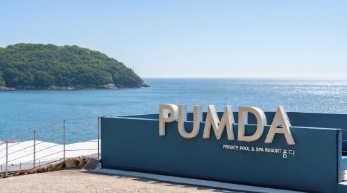 a sign for a pumbaa company in front of the ocean at Namhae Pumda Pool villa Pension in Namhae