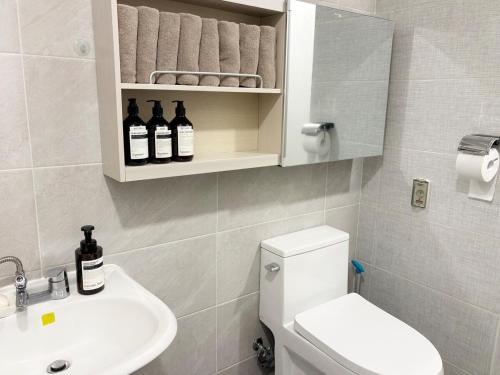 a bathroom with a toilet and a sink with bottles on a shelf at 깨비하우스201 in Wŏlsan