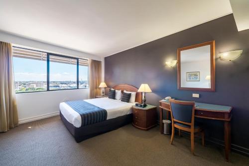 a hotel room with a bed and a desk and a mirror at Great Southern Hotel Brisbane in Brisbane