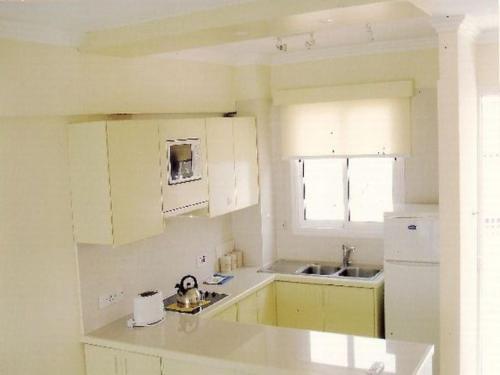 Paphinia SeaView Apartments في بافوس: مطبخ صغير مع دواليب بيضاء ومغسلة