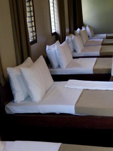 a row of four beds with white sheets and pillows at Sheridan Organic Farm and Resort in Maratapi