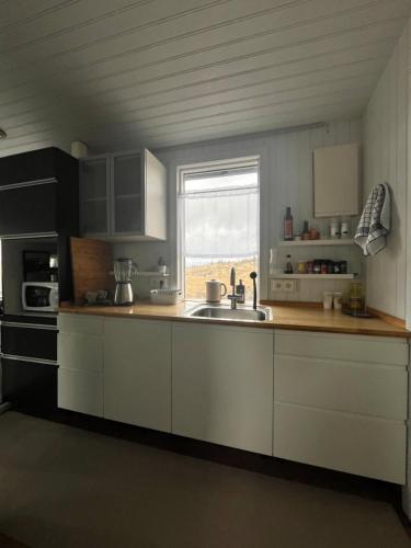 a kitchen with white cabinets and a sink and a window at Cozy Cabin Iceland in Reynivellir
