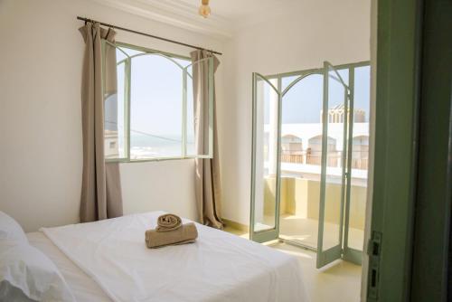 a bed with a towel on it in a room with windows at Sand House in Imsouane