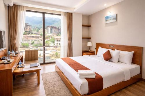 ein Schlafzimmer mit Bett, Schreibtisch und einem großen Fenster in der Unterkunft Hotel HTC , Thimphu in Thimphu