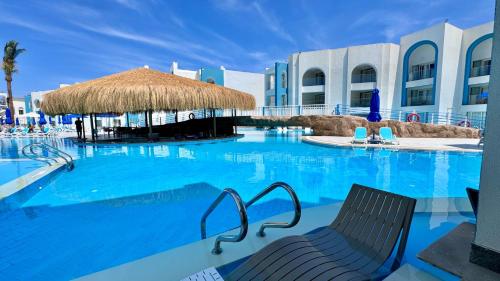 a large swimming pool with two chairs and a straw umbrella at Stella Beach Resort & Spa Makadi Bay - 24 HRS All Inclusive in Hurghada