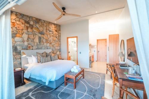 a bedroom with a stone wall with a bed and a desk at Whale Coast Luxury Suites in Hermanus