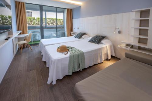 a hotel room with two beds and a hat on a table at GHT Sa Riera in Tossa de Mar