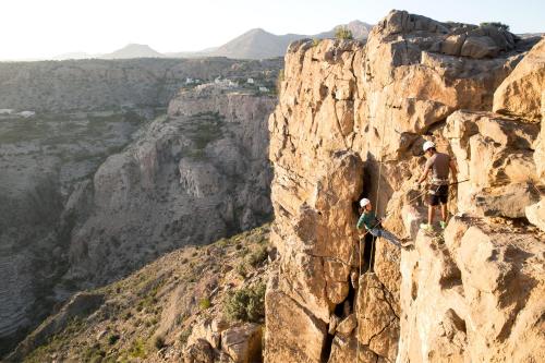 two people are climbing on a rock cliff at Anantara Al Jabal Al Akhdar Resort in Al ‘Aqar