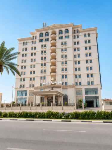 a large white building with a palm tree in front of it at Golden Tulip Al Khobar in Al Khobar