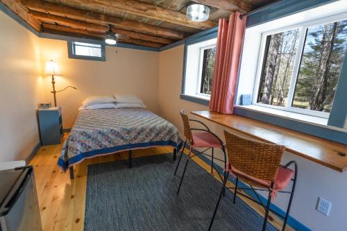 a bedroom with a bed and two chairs and two windows at The ShackHilton at Dancing Light Farm in Bridgton