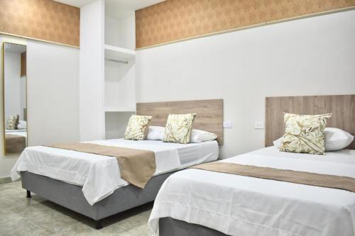 two beds in a bedroom with white walls at Hotel Santo Rio Suite Santa Marta in Santa Marta