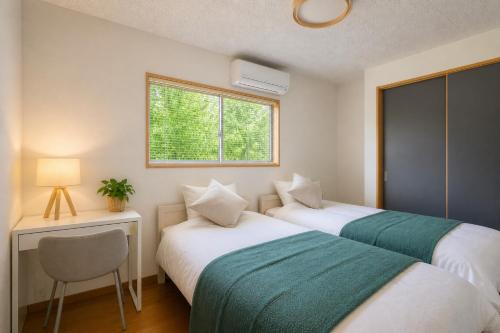 two beds in a room with a desk and a window at Aso Vista in Aso