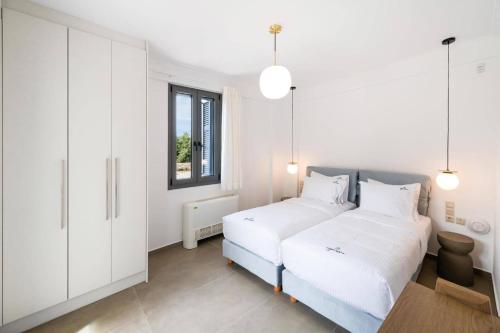 a white bedroom with two beds and a window at Villa Cypressa by Villa Plus in Kalamitsi