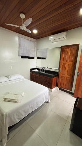 a bedroom with a white bed and a kitchen at Suítes Aymoré in Itacaré