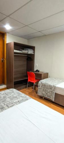 a bedroom with two beds and a desk and a red chair at Hotel La Costa in Rio de Janeiro