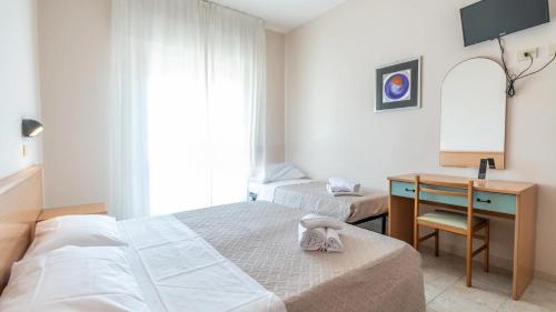 a bedroom with two beds and a desk with a mirror at Hotel Anny in Cervia