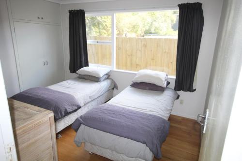 two beds in a room with a window at Waiwera Beach GetAway in Waiwera